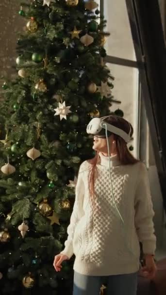Μια όμορφη νεαρή κοπέλα εξερευνά ένα χριστουγεννιάτικο δέντρο μέσα από γυαλιά εικονικής πραγματικότητας. Υψηλής ποιότητας 4k πλάνα - Πλάνα, βίντεο