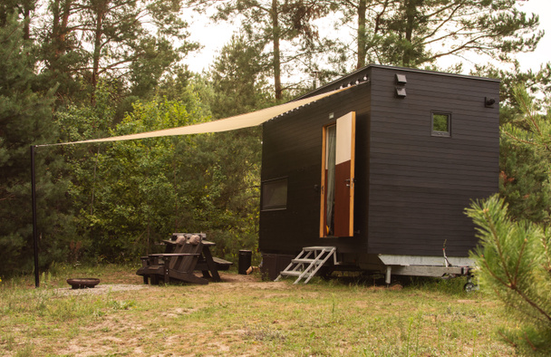 Un apartamento modular de tipo marco sobre ruedas, forrado con madera sobre el fondo de un bosque otoñal. Espacio ecológico móvil para vivir y turismo. - Foto, imagen