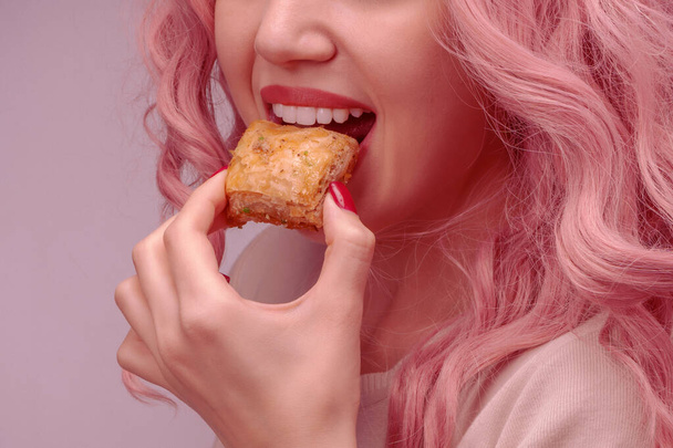 Γυναίκα με ροζ σγουρά μαλλιά τρώει μπακλαβά από κοντά.. - Φωτογραφία, εικόνα