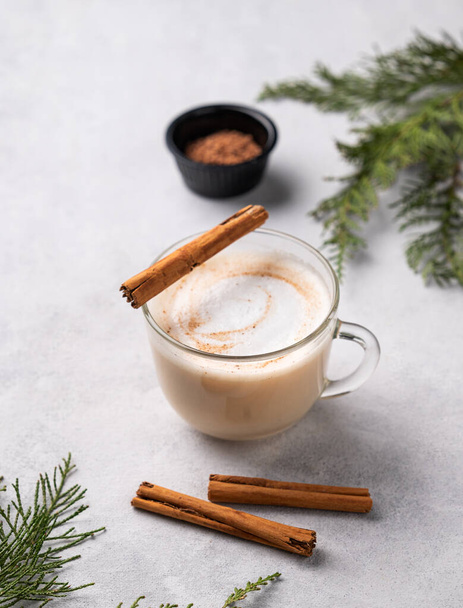 Kořeněné kávové latté nebo cappuccino se skořicovými tyčinkami na lehkém pozadí s jedlovými větvemi. Koncept vánočního ohřívacího nápoje. Slavnostní zimní nálada.  - Fotografie, Obrázek