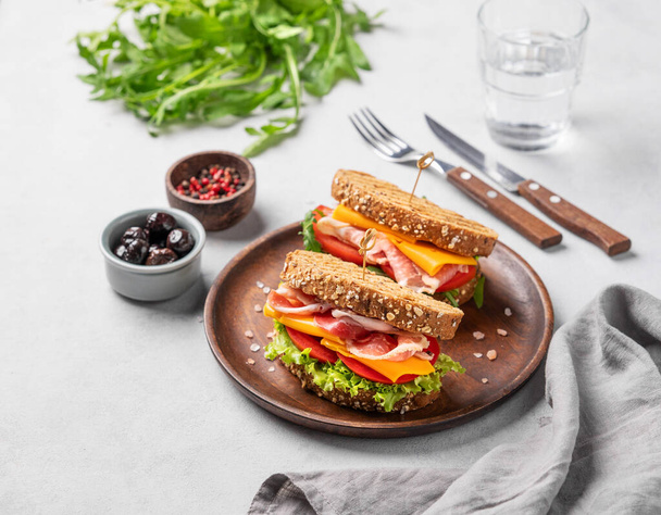 Twee toast club sandwiches gemaakt van graan brood met cheddar kaas en spek gevuld met tomaten en sla en arugula op een houten plaat op een lichte achtergrond. Gezond ontbijt concept.  - Foto, afbeelding