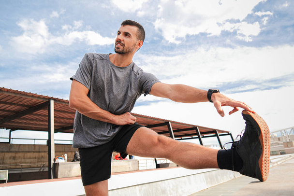 Активный спортсмен растягивает ноги после тренировки. Спортсмен восстановить свои мышцы в фитнес-тренировки рутины, имеющие здоровый образ жизни. Парень делает ежедневные силовые упражнения - Фото, изображение
