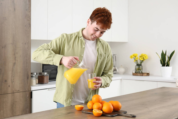 Genç adam mutfakta portakal suyunu bardağa dolduruyor. - Fotoğraf, Görsel