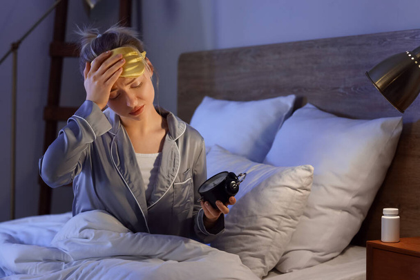 Álmos fiatal nő ébresztőórával a hálószobában éjjel - Fotó, kép