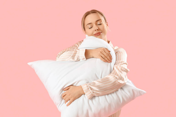 Junge Frau im Schlafanzug mit Kissen auf rosa Hintergrund - Foto, Bild