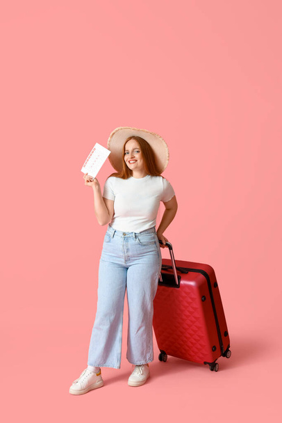 Young woman with menstrual calendar and suitcase on pink background - Photo, Image