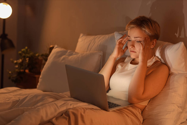 Сонная молодая женщина, использующая ноутбук в постели ночью - Фото, изображение