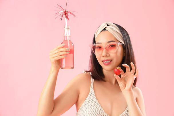 Beautiful Asian woman in swimsuit and with strawberry drink on pink background - Photo, Image