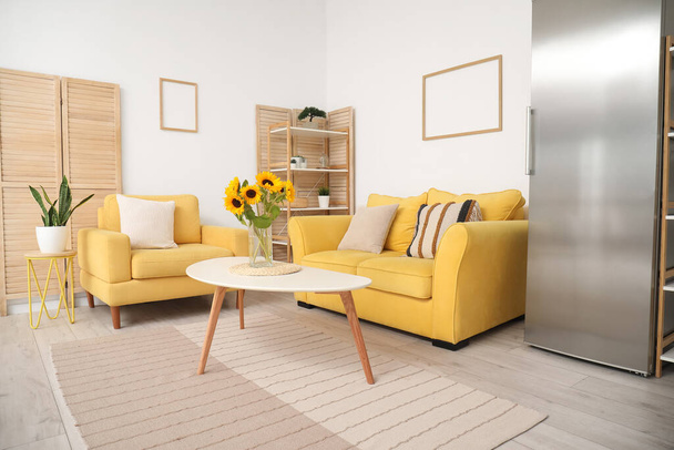 Vase with beautiful sunflowers, yellow sofa and armchair in interior of stylish living room - Photo, Image