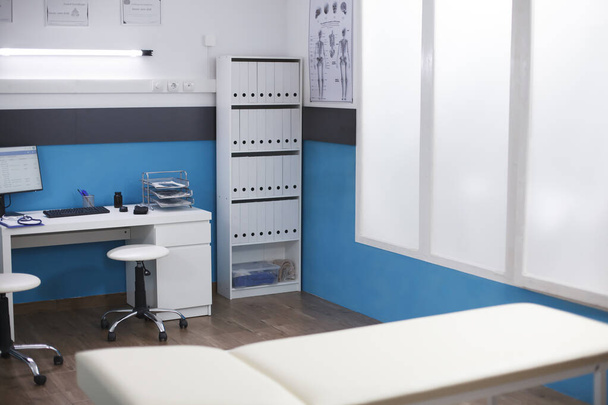 Obrázek představuje klinickou kancelář, která se používá pro konzultace a schůzky. Prázdný nemocniční pokoj obsahující stůl s počítačem pro lékaře a vyšetřovací lůžko. - Fotografie, Obrázek