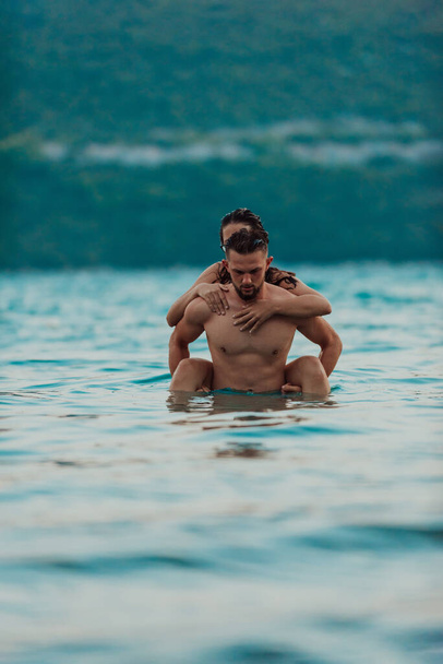 Um jovem casal romântico compartilhando um beijo apaixonado em meio à beleza serena do oceano ao pôr do sol - Foto, Imagem