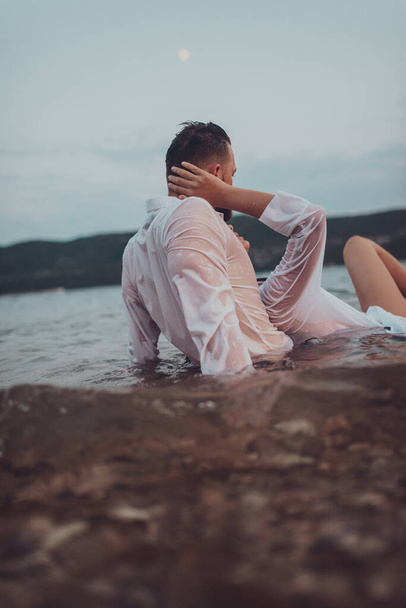 日没の静かな海の美しさの中で情熱的なキスを共有するロマンチックな若いカップル - 写真・画像