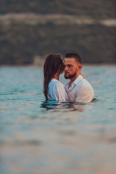 Ένα συμβολικό και συναισθηματικά συνδεδεμένο ζευγάρι αγκαλιάζει τρυφερά το φόντο μιας γαλήνιας θάλασσας, λουσμένο στις ζεστές αποχρώσεις ενός μαγευτικού ηλιοβασιλέματος.  - Φωτογραφία, εικόνα