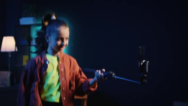 Smartphone en selfie stick usado por el talentoso niño z gen en cuarto oscuro haciendo coreografía de baile viral, creando contenido para generar vistas y engagement de otros niños en línea - Metraje, vídeo