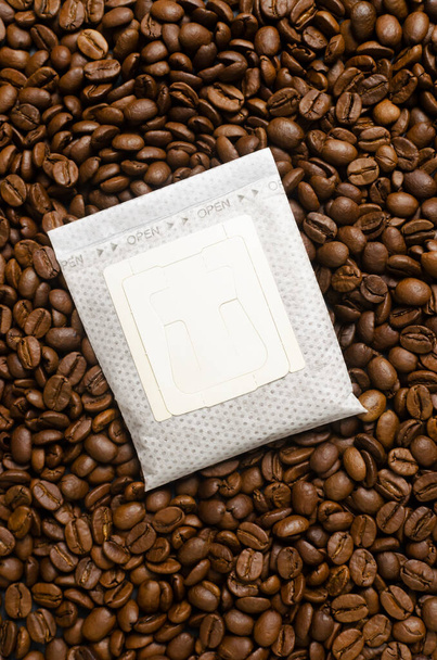 Kaffeetüte auf einen Hintergrund aus Bohnen tropfen lassen. Eine schnelle Möglichkeit, ein schmackhaftes und aromatisches Getränk zuzubereiten. Vertikale Orientierung. Ansicht von oben - Foto, Bild