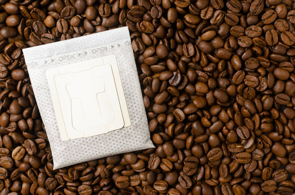 Kaffeetüte auf einen Hintergrund aus Bohnen tropfen lassen. Eine schnelle Möglichkeit, ein schmackhaftes und aromatisches Getränk zuzubereiten. Horizontale Ausrichtung. Ansicht von oben. Kopierraum - Foto, Bild