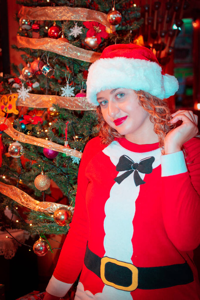 Feliz Navidad y Feliz Año Nuevo. Retrato de una hermosa joven vestida con ropa de Santa Claus cerca del árbol de Navidad. en casa - Foto, imagen