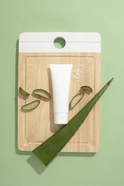 Draufsicht auf eine leere Plastikröhre und frische Aloe-Vera-Blätter auf einem Holzschneidebrett. Kosmetikkonzept mit natürlichen Extrakten - sicher und gut für die Haut. - Foto, Bild