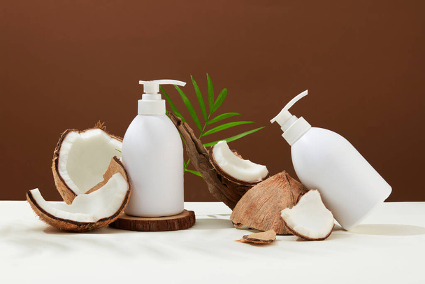 Немічені гелеві пляшки для душу, що містять кокосовий екстракт, демонструються з кокосовими пластівцями різного розміру. Мінімалістичний фон з темою краси. - Фото, зображення