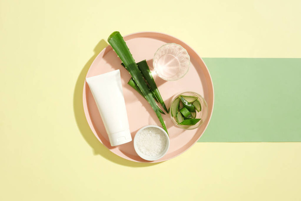 Egy cső márkátlan arctisztító és kellékek jelennek meg egy rózsaszín kerámia lemez. Az Aloe vera magas fahéjsavszintet tartalmaz, amely fertőtlenítő hatással van a bőrre, és megelőzi a gyulladást - Fotó, kép