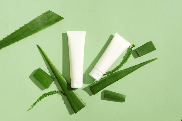 Dos tubos blancos de limpiador facial decorados con aloe vera fresco sobre un fondo verde. Cosméticos caseros con ingredientes naturales ayudan a tratar y restaurar la piel. - Foto, imagen