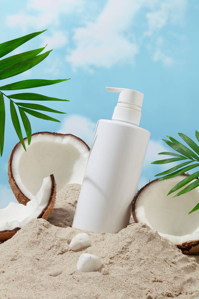 Unbranded douchegel fles en verse kokosnoot op zandstrand tegen een levendige blauwe lucht. Stralende zomerse vibes, de essentie van een tropisch paradijs in een advertentie. - Foto, afbeelding