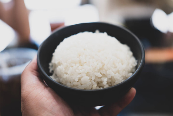 Hands holding a black bowl of rice. - Photo, Image