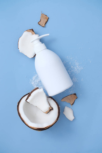 Botella cosmética blanca de champú, jabón o gel de ducha con un dispensador sobre el fondo azul de un coco roto. Mockup para anuncios cosméticos. Visto desde arriba. - Foto, imagen