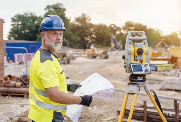 Een man site engineer landmeter werken met theodoliet totale station EDM-apparatuur op een bouwplaats buiten - Foto, afbeelding