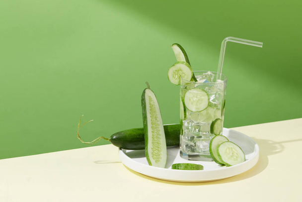 A glass containing fresh cucumber slices and ice is placed on a white ceramic plate. Cucumbers contain 95% - 97% water combined with minerals to help replenish and retain water for the body. - Photo, Image