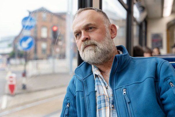 Porträt eines verträumten bärtigen Mannes in blauer Jacke in einem Bus. Lifestyle-Konzept - Foto, Bild