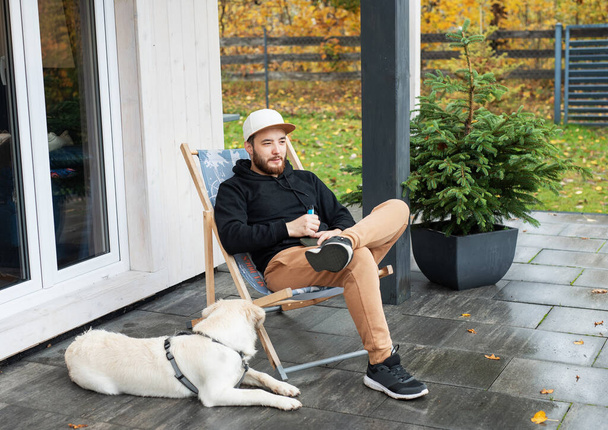 Young man sitting with golden retriever on terrace - Photo, Image