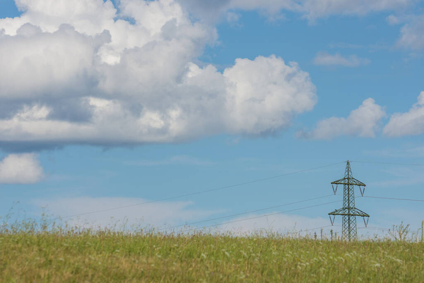 einzelner Strommast grünes Gras und weiße Wolken am blauen Himmel - Foto, Bild