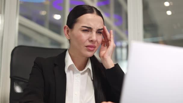 Zdenerwowana kobieta przedsiębiorca siedzi i patrząc na nowoczesny ekran laptopa, czując silny ból głowy w jasnym biurze. Dorosła kobieta biznesu pracy i masażu świątynie z rąk w miejscu pracy. - Materiał filmowy, wideo