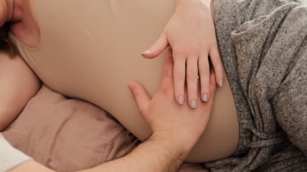 Zwangere paar van man en vrouw aanraken buik en voelt liefde en ontspannen thuis. Jonge zwangere vrouw die zwanger is. Vader zorgt voor zwangere moeder. Begrip moederschap en - Video