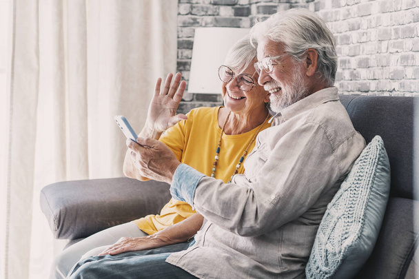 Happy retired family couple using mobile phone for video call together, talking to relations, getting good news, having fun, smiling and laughing. Carefree mature pensioners chatting online on cell - Photo, Image