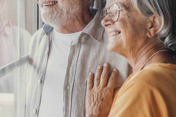 Happy bonding liefdevolle middelbare leeftijd senior gepensioneerde paar staan in de buurt venster, kijken in de verte, herinneren van goede herinneringen of het plannen van gemeenschappelijke toekomst, genieten van rustige moment samen thuis. - Foto, afbeelding