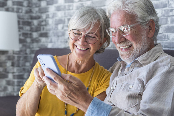 Starszy dziadek i babcia spędzają czas bawiąc się za pomocą aplikacji na smartfony, żona w średnim wieku cieszyć się rozrywkami online, robiąc selfie ze starym mężem, starszym pokoleniem i nowoczesną koncepcją technologii - Zdjęcie, obraz