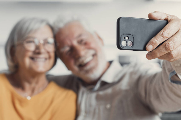 Happy old couple taking selfie on cellphone, smiling senior mature spouses middle aged wife and retired husband laughing holding phone make self portrait on smartphone camera, focus on mobile display - Photo, Image