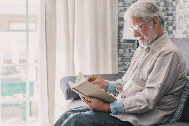 自宅で本を読んで座っている老人の幸せとリラックスした男の近くにヘッドショットの肖像画。熟女男性楽しい時間を楽しんで屋内. - 写真・画像