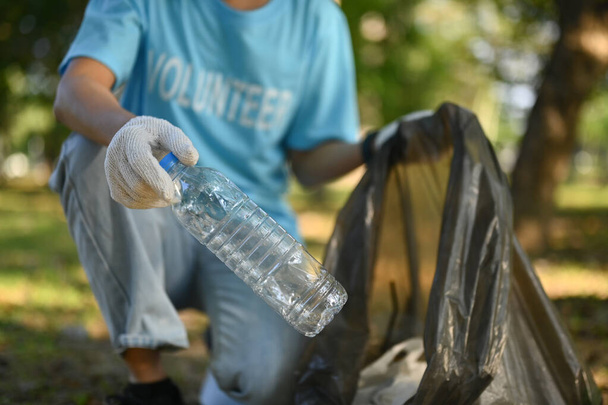 Молода жінка-доброволець збирає пластикову пляшку в парку. Концепція захисту навколишнього середовища. - Фото, зображення