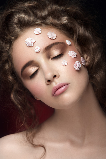 Romantic nude young beautiful girl with white flowers on her face and soft curls on dark background. - Foto, afbeelding