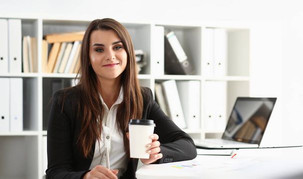 Beautiful young businesswoman holding glass of coffee at workplace. Break and rest in office concept - Photo, Image
