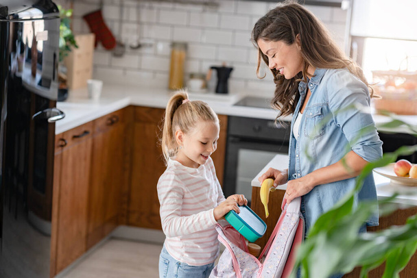 mother and daughter packing lunch into school bag - Photo, Image