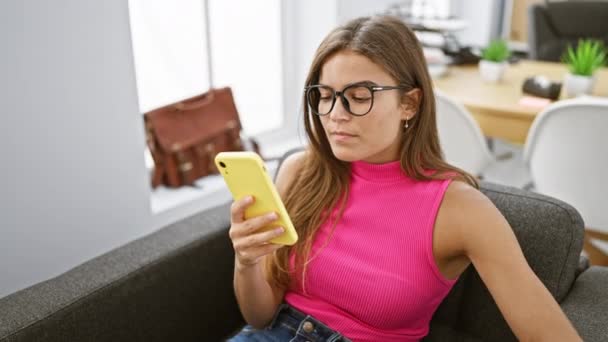Attractive young hispanic woman deep in thought, holding her smartphone while working at her office job, exhibiting her successful, professional side in an elegant indoor setting. - Footage, Video
