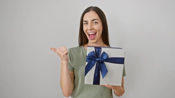 Fröhliche junge hispanische Frau zeigt selbstbewusst ihr Geburtstagsgeschenk, Daumen zeigt gute Stimmung zur Seite, isoliert auf weißem Hintergrund. - Filmmaterial, Video