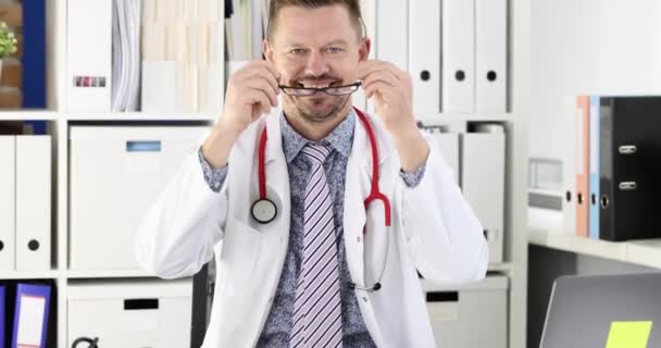 Man arts neemt af bril voor visie en kruising armen in het kantoor van kliniek 4k film slow motion. Professioneel concept van medisch advies - Video