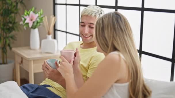 Gyönyörű pár iszik egy csésze kávét ül az ágyon a hálószobában - Felvétel, videó