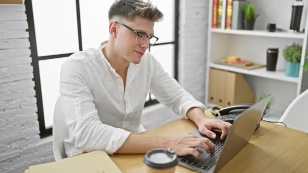 Szczęśliwy i pewny siebie, młody biały mężczyzna pracujący nad laptopem w biurze. pracownik biznesu gwoździ swoją pracę z niezachwianą pewnością siebie i uśmiechem na twarzy. - Materiał filmowy, wideo