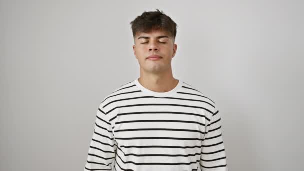 Handsome young hispanic man relaxing, closing eyes for zen yoga and meditation in striped casual gear, portraying healthy wellness concept. isolated white cutout background - Footage, Video